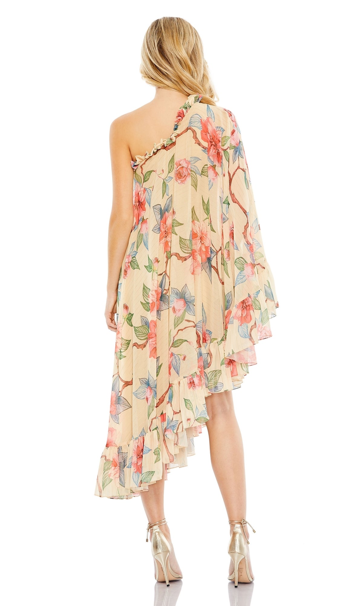A woman stands with her back to the camera wearing the Mac Duggal Long Formal Dress 55830, a one-shoulder gown with a floral print and ruffled hem, paired with metallic high-heeled shoes.